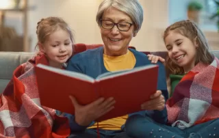 grandmother reading a red book to two girls in a snuggly blanket