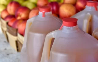 apple cider in gallon jugs in front of baskets of fresh apples